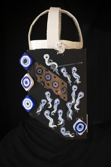 On a black background is a form covered with evil eye depictions with a white arched shape at the top