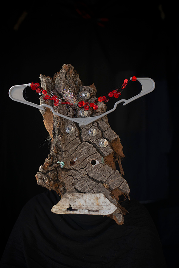 A masking consisting of a large piece of bark with a a portion of a grey hanger and a string of red mylar pieces.