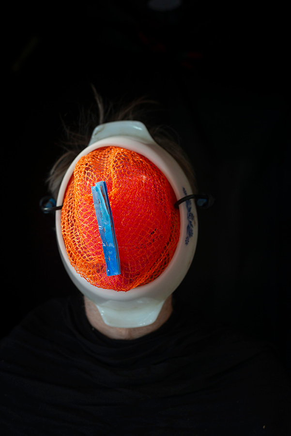 Out of a black background emerges a white oval with an orange netting at its center.