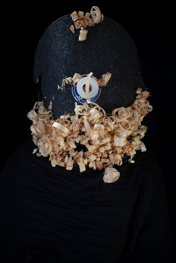 A largely black form accented with a beard of pale wood shavings on a black background.