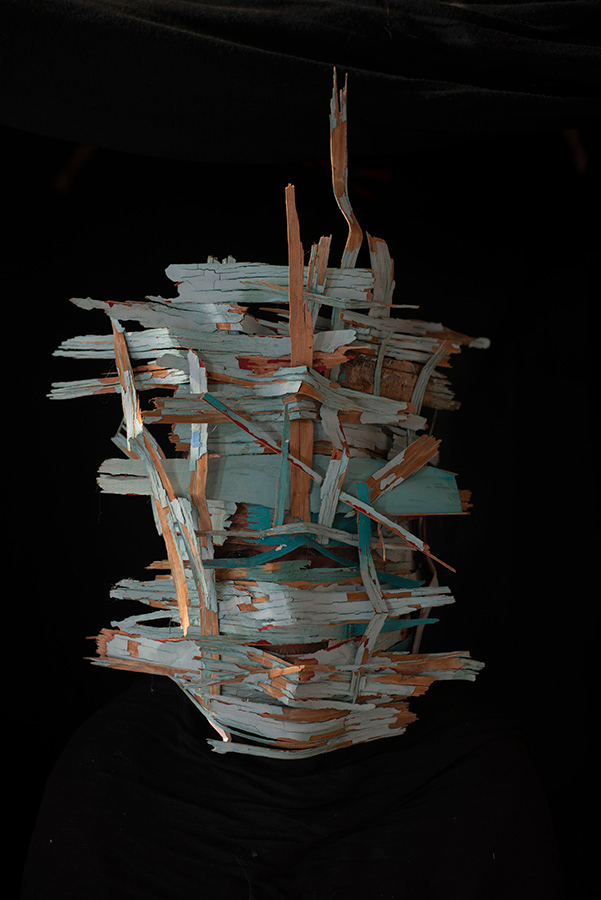 A mask of woven strips of wood partially painted turquoise.