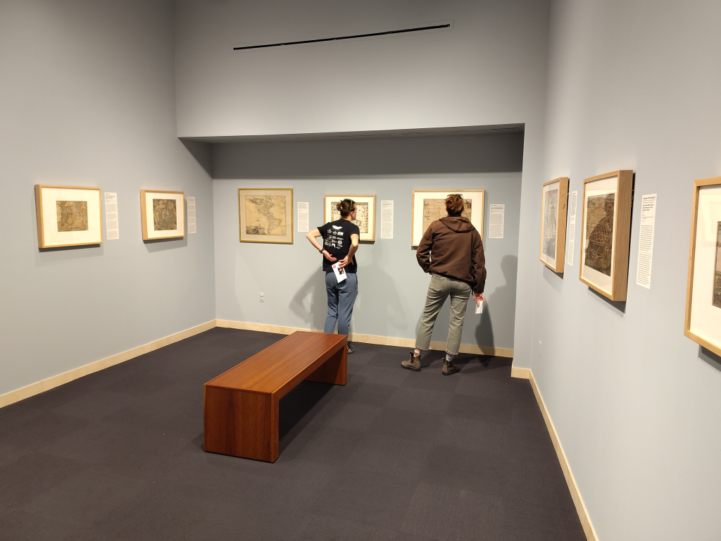 A view of the backs of two people as they look at an exhibit of maps