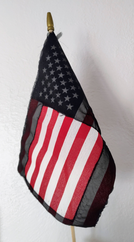 An American flag shrouded in a translucent black fabric with a rectangle of four white and five red stripes left uncovered.